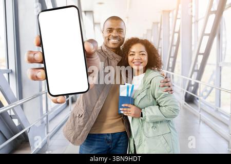 Black couple at airport holding smartphone with blank screen and boarding passes Stock Photo