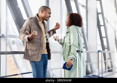 Young Black couple arguing in airport, having intense conversation Stock Photo