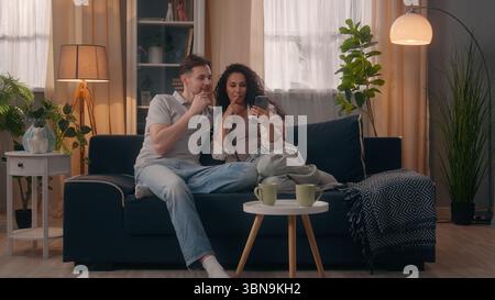 Smiling multiracial couple multiethnic Caucasian man male guy husband with Hispanic woman female girl wife shopping mobile phone together talking Stock Photo