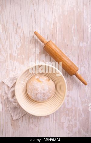 Raw yeast dough with rolling pin resting and rising in a special basket on kitchen table Stock Photo