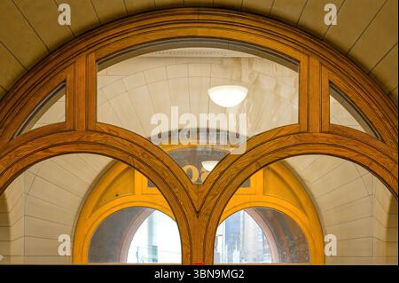 A large arched transom window at Old City Hall features wooden framing with symmetrical curved muntins, set within a stone wall and reflecting interio Stock Photo