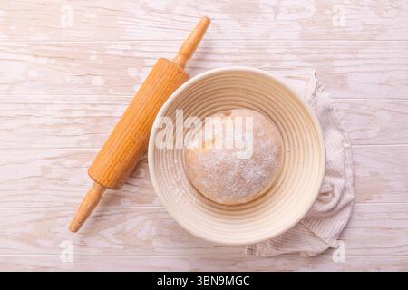 Raw yeast dough with rolling pin resting and rising in a special basket on kitchen table Stock Photo