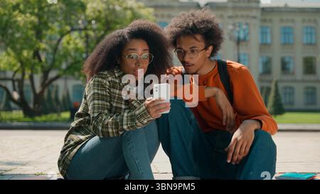 African American couple man woman friends students male female girl guy together in city outdoors looking mobile phone using smartphone reading bad Stock Photo