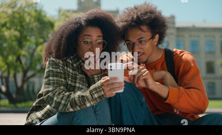 African American couple man woman friends students male female girl guy together in city outdoors looking mobile phone using smartphone reading bad Stock Photo