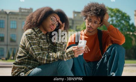 African American couple man woman friends students male female girl guy together in city outdoors looking mobile phone using smartphone reading bad Stock Photo