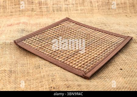 Square handmade woven placemat on burlap fabric, rustic natural background for kitchen, dining, table setting, eco decor and cozy home interior. Stock Photo