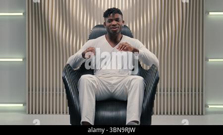 African American guy man ethnic male putting wireless headphones in ears listening music dancing waving arms moving hands dance to audio song in Stock Photo