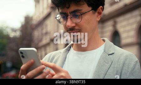 Serious concentrated Indian ethnic business man using mobile phone in city texting chatting message smartphone app internet online guy businessman Stock Photo