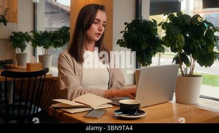 Caucasian business woman laptop working remote writing notes sitting in cafe chatting with clients internet female freelancer girl at cafeteria table Stock Photo