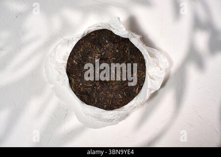 A round, compressed puer tea is showcased on a piece of white paper ...
