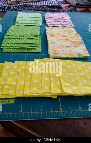 Close-up of a collection of cut quilting squares sorted into separate piles on a cutting mat on a wooden table. Stock Photo