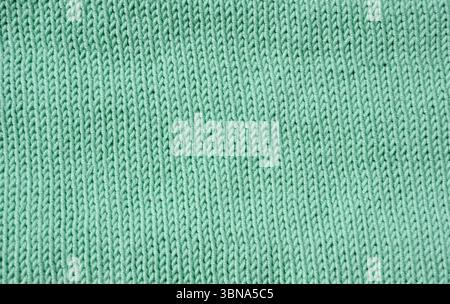 A detailed macro shot shows a mint green knit fabric. The stockinette stitch with neat vertical V-shaped patterns creates a soft, even and textured su Stock Photo