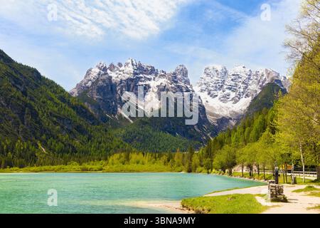 Vibrant turquoise waters of Lago di Landro, set against the dramatic backdrop of snow-capped Cristallo mountain peaks and lush green forests under a b Stock Photo