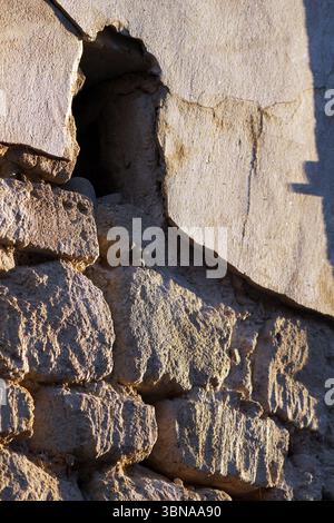 Nicosia (Lefkosia), Cyprus, the world’s last divided capital, A close-up view of a weathered stone wall. The wall is constructed of large, irregularly shaped stones in shades of gray and beige, with some areas showing signs of age and weathering. A small, rectangular opening is visible in the wall, possibly a window or a natural opening. The wall is made of rough, uneven stones, and the perspective of the image is from below, looking up at the wall. The wall shows signs of damage and wear, with cracks and crevices visible. The lighting in the image is bright, possibly indicating sunlight, and Stock Photo