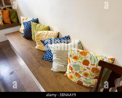 A wooden bench with pillows on it. There are six pillows on the bench. The pillows are in different colors and patterns Stock Photo