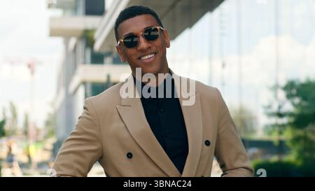 Smiling stylish fashionable confident African American business man posing in city outdoors wearing black sunglasses businessman guy male entrepreneur Stock Photo