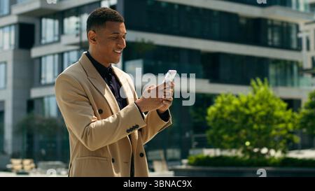 Happy smiling handsome African American ethnic male entrepreneur employer guy business man using online mobile phone smartphone typing app message Stock Photo