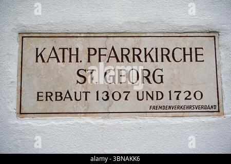 Schärding, the charming Baroque gem by the Inn River in Upper Austria. Known for the colorful Baroque “Silberzeile” row of pastel guild houses and well-preserved medieval walls & gates., A rectangular stone plaque affixed to a white wall. The plaque is inscribed with the name "KATH. PFARRKIRCHE ST. GEORG" in a serif font, followed by "ERBAUT 1307 UND 1720" in a sans-serif font. The text is set within a dark brown or black border. At the bottom of the plaque, the words "FREMDENVERKEHRSVERBAND" are inscribed in a smaller font. The plaque appears to be made of a light-colored stone, possibly Stock Photo