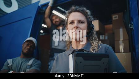 Portrait of Multiethnic Employees Standing Outside of Logistics Retail Warehouse, Looking at Camera. Delivery Truck Full of Cardboard Boxes with Online Orders. Female Manager Holding Tablet Computer. Stock Photo