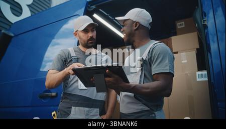 Multiethnic Workers Standing near Delivery Truck Full of Cardboard Boxes with Online Orders Ready for Shipment. African American Manager Using Tablet Computer. Outside of Logistics Retail Warehouse. Stock Photo