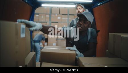Multiethnic Workers Scanning Cardboard Boxes with Online Orders, E-Commerce Goods in Delivery Truck Using Barcode Scanner, Checking Details on Tablet Computer. Outside of Logistics Retail Warehouse. Stock Photo