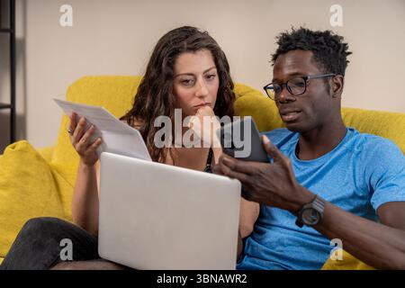 couple, working from home, laptop, home, together, focused, studying, e-learning, business, man, woman, young adult, diversity, multiethnic, relations Stock Photo