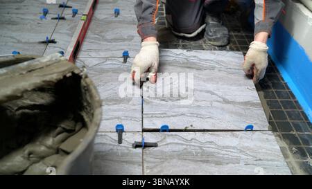 Professional construction worker carefully laying ceramic floor tiles using cement adhesive, showcasing precise tiling technique in interior renovatio Stock Photo