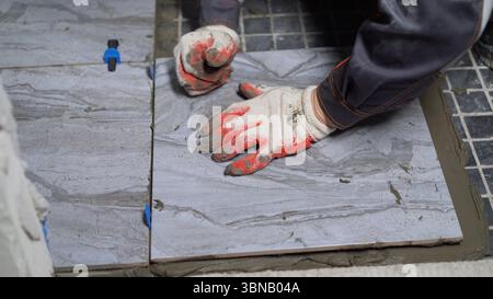 Professional construction worker carefully laying ceramic floor tiles using cement adhesive, showcasing precise tiling technique in interior renovatio Stock Photo