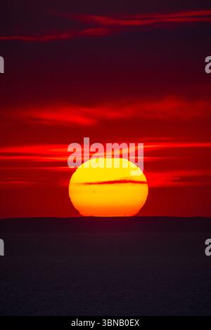 Vibrant red sunset over the sea horizon with a dark silhouette of distant hills. Stock Photo