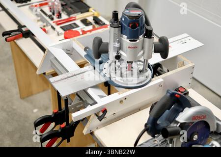 High-precision woodworking using a plunge router and other power tools in a workshop environment. Captured indoors with artificial light. Stock Photo