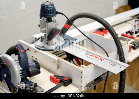 High-precision woodworking using a plunge router and other power tools in a workshop environment. Captured indoors with artificial light. Stock Photo