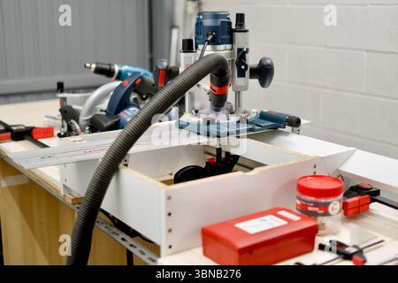 High-precision woodworking using a plunge router and other power tools in a workshop environment. Captured indoors with artificial light. Stock Photo