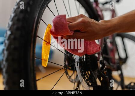 Close-up hands of unrecognizable cyclist cleaning spokes and reflector of dirty bicycle wheel with microfiber cloth, ensuring bike in top condition at Stock Photo