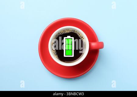 Cup of coffee with fully charged battery indicator on light blue background, top view. Restoring energy with caffeine Stock Photo