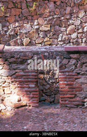 Rustic stonework features a weathered arch surrounded by a mix of stones in warm tones. Stock Photo