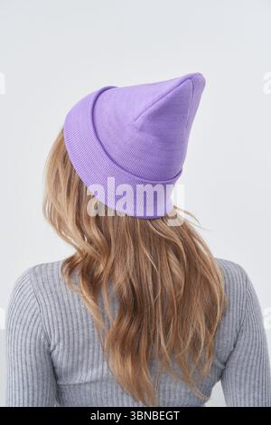 Woman with long wavy hair wearing a light purple knitted beanie and a gray ribbed sweater. The image captures the back of her head and upper body in a Stock Photo