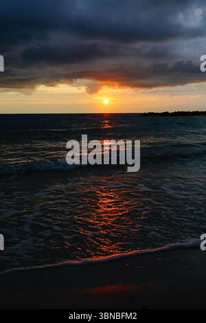 As the sun sets light reflects off waves in the water with storm clouds rolling in overhead. Stock Photo