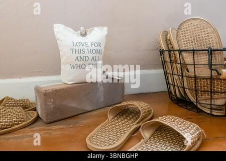 a welcoming message, "Love for this home and all who enter". slippers, a doorstop, and a brick, conveying a cozy and inviting ambiance. Thailand Stock Photo
