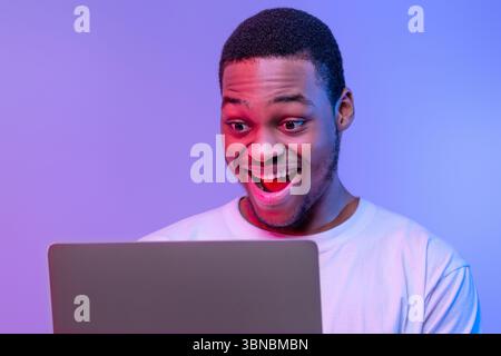 Closeup Shot Of Excited Black Guy Using Laptop Computer Under Neon Lighting Stock Photo