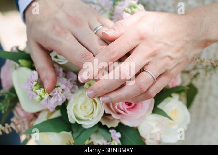 Two hands display wedding rings while holding a vibrant floral bouquet during a joyful outdoor ceremony. Stock Photo