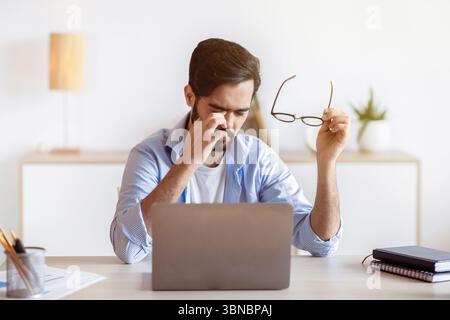 Eye Strain. Tired Arab Freelancer Guy Feeling Exhausted After Working On Laptop Stock Photo