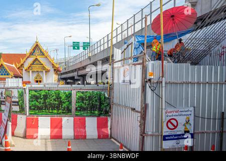Workers under umbrella, construction site with barriers beside a traditional Thai building, under highway, Bangkok Noi, Thailand Stock Photo