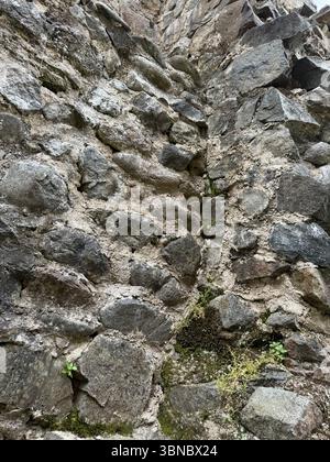 This photo shows a vertical segment of a weathered stone wall, built using large irregular stones and filled with aged mortar. The wall exhibits signs Stock Photo