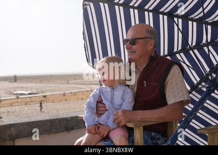 An elderly Spanish man sits with his granddaughter under a parasol on a promenade  Stock Photo