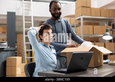 Diverse storehouse employees working together to process custom orders and manage inventory, e commerce delivery service. Team of people packing merchandise in the storage room depot. Stock Photo