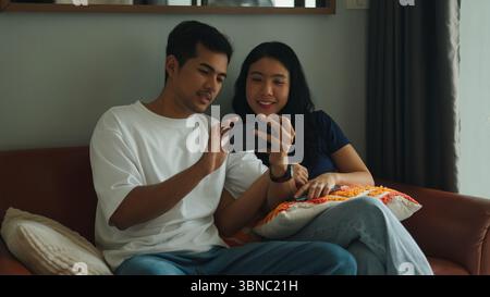Happy couple using mobile phone at home, enjoying time together Stock Photo