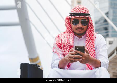 Islamic man using smartphones app organize schedule agenda  focus on hands holding smartphone muslim modern uae city. Arab men wear hijab and muslim f Stock Photo