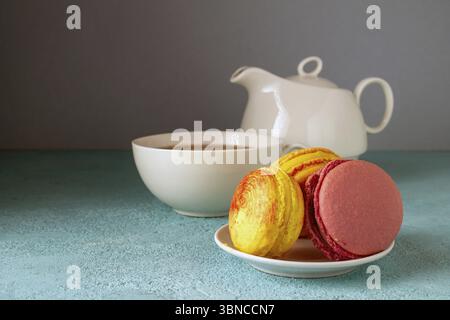 Colored macaroons and a teapot with a cup on a blue table Stock Photo