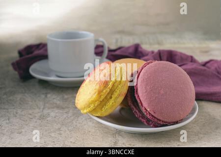 French dessert - macaroons, coffee cup, lilac napkin on beige table Stock Photo