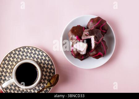 Plate with chocolate marshmallows and a cup of coffee on a pink background Stock Photo